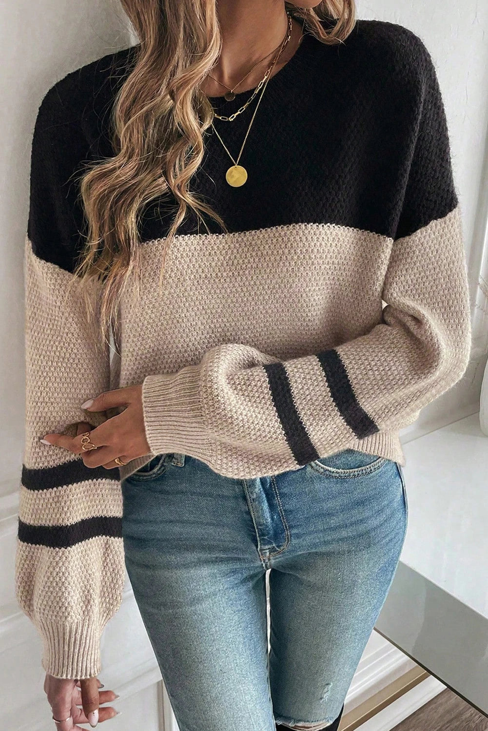 Person wearing a black and beige sweater with blue jeans indoors.