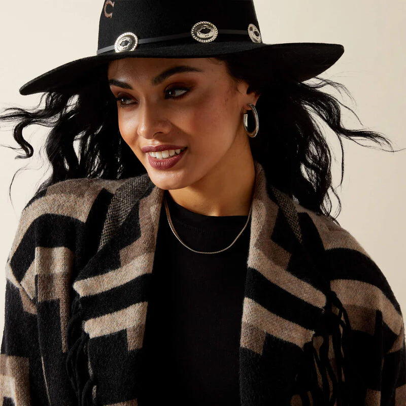 Woman wearing a black hat with decorative elements and a patterned cardigan.