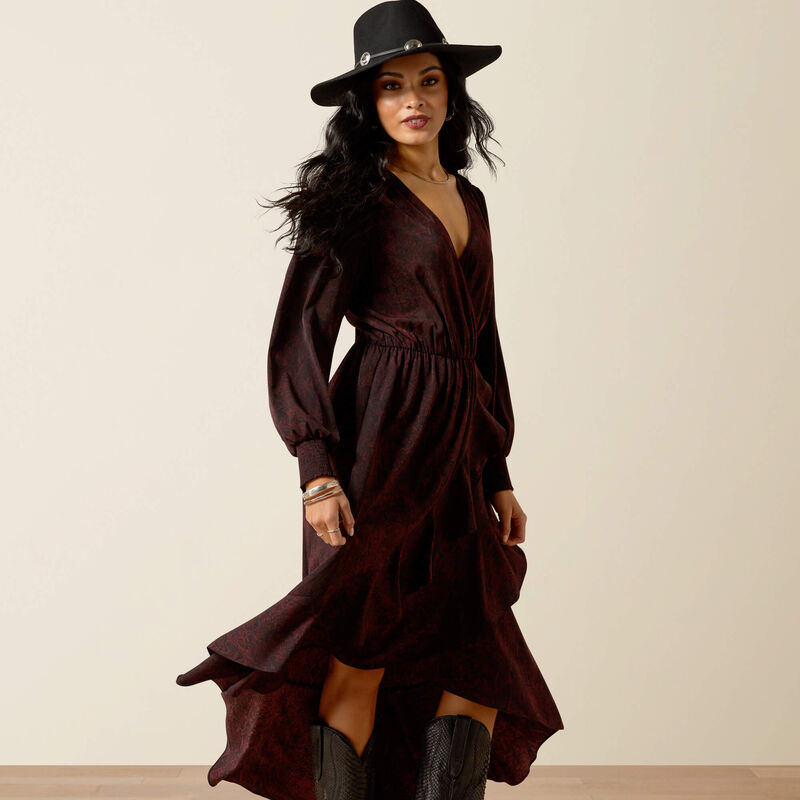 Woman wearing a dark brown dress and black hat against a beige background