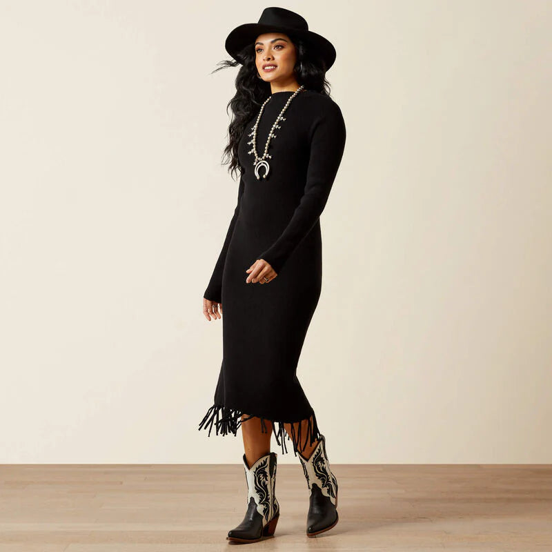 Woman wearing a black dress with fringe, black hat, and cowboy boots on a beige background