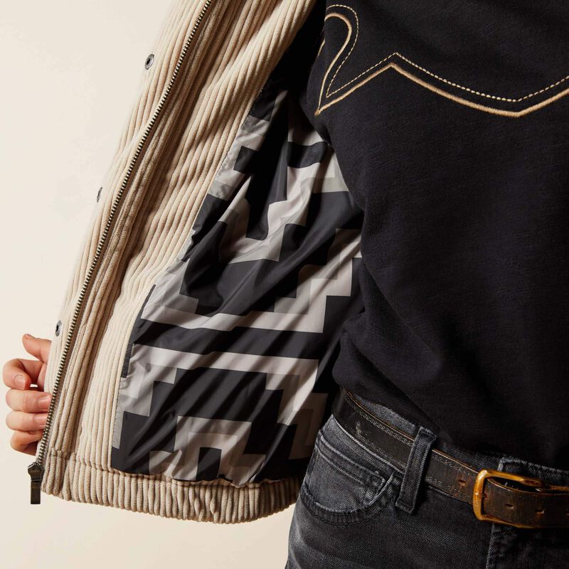 Close-up of a person wearing a beige jacket with a patterned lining, black shirt, and jeans.