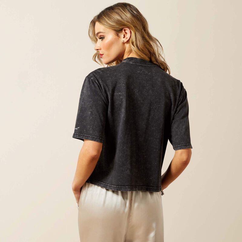 Woman wearing a black t-shirt and beige pants against a plain background