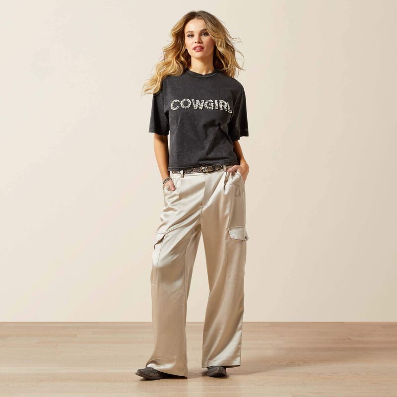 Woman wearing a black 'COWGIRL' t-shirt and beige pants on a plain background