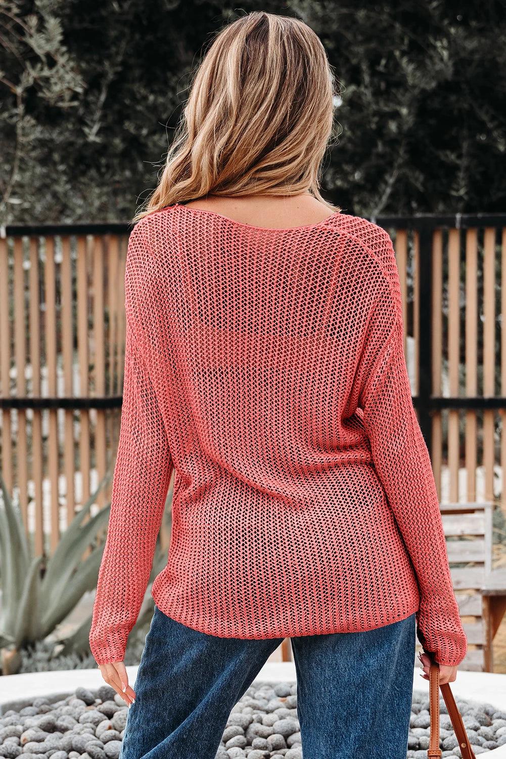 Person wearing a pink knit sweater and blue jeans standing outdoors.