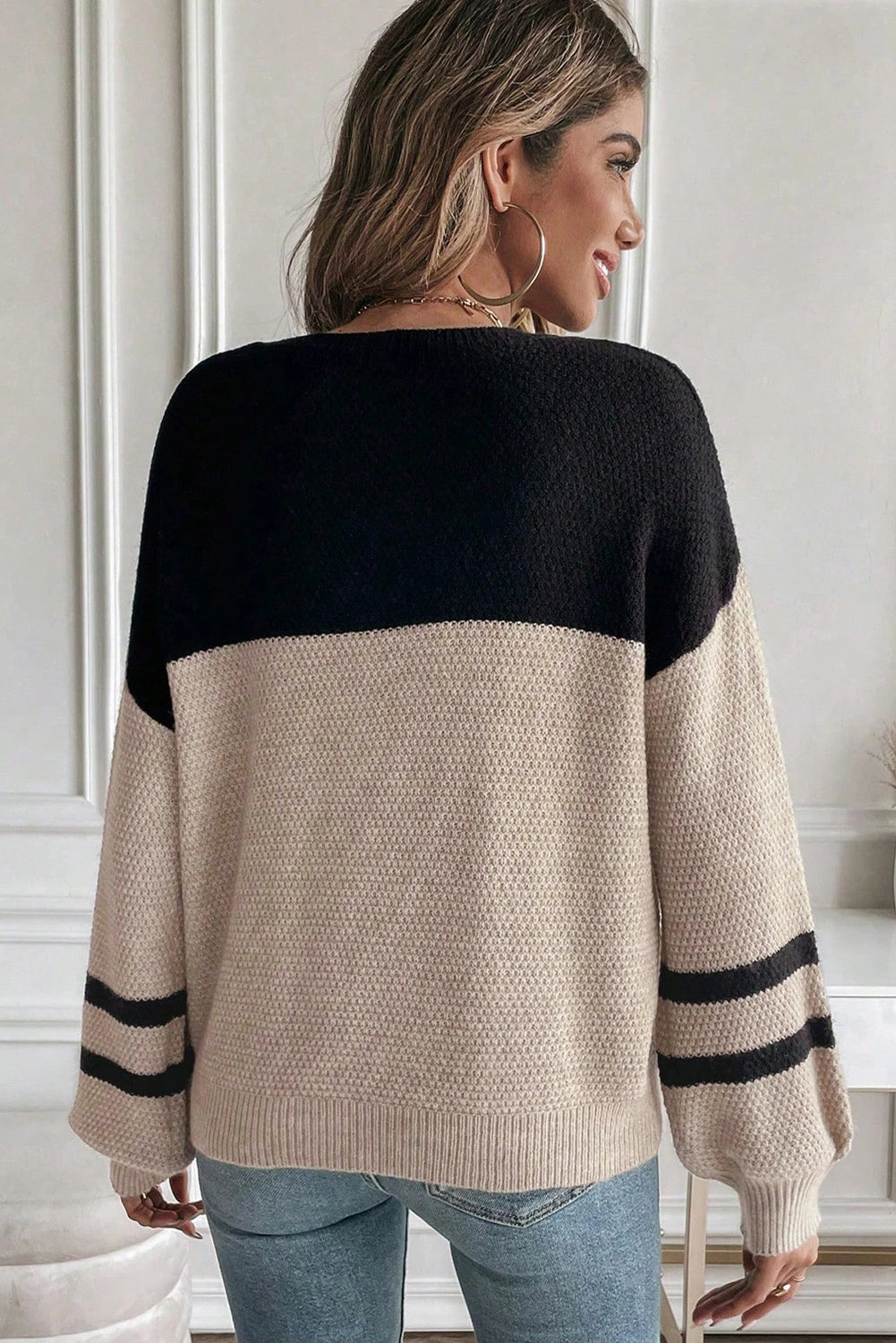 Woman wearing a black and beige sweater with striped sleeves indoors.