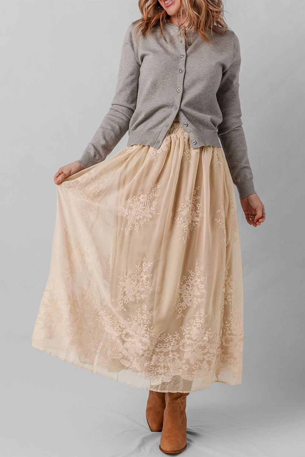 Woman wearing a gray cardigan and beige lace skirt on a plain background