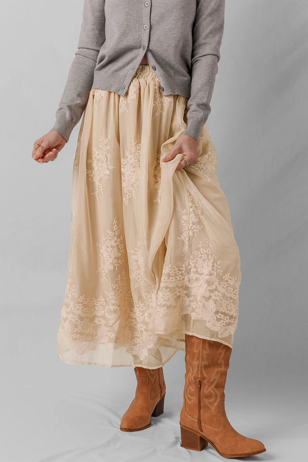 Person wearing a beige lace skirt with brown boots on a plain background