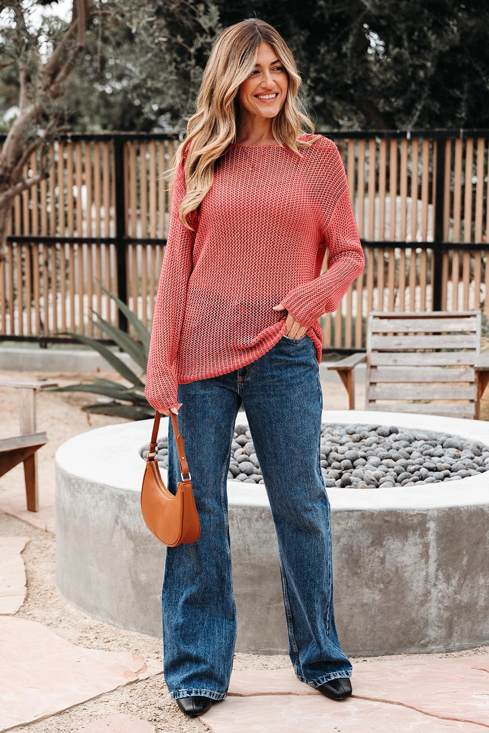 Woman wearing a pink sweater and blue jeans standing outdoors near a stone wall.