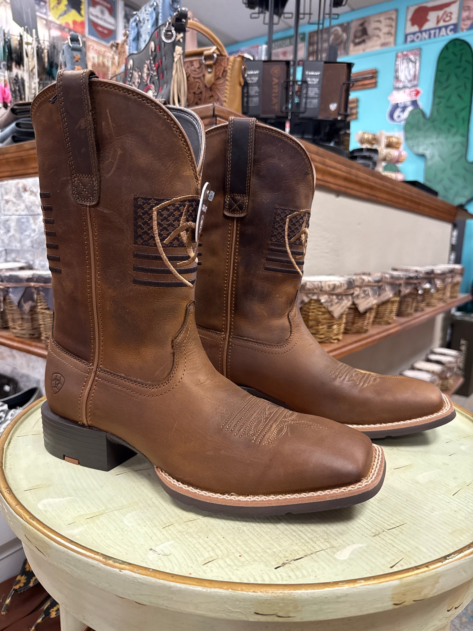 Brown leather boots with a decorative buckle on a wooden barrel in a store setting.