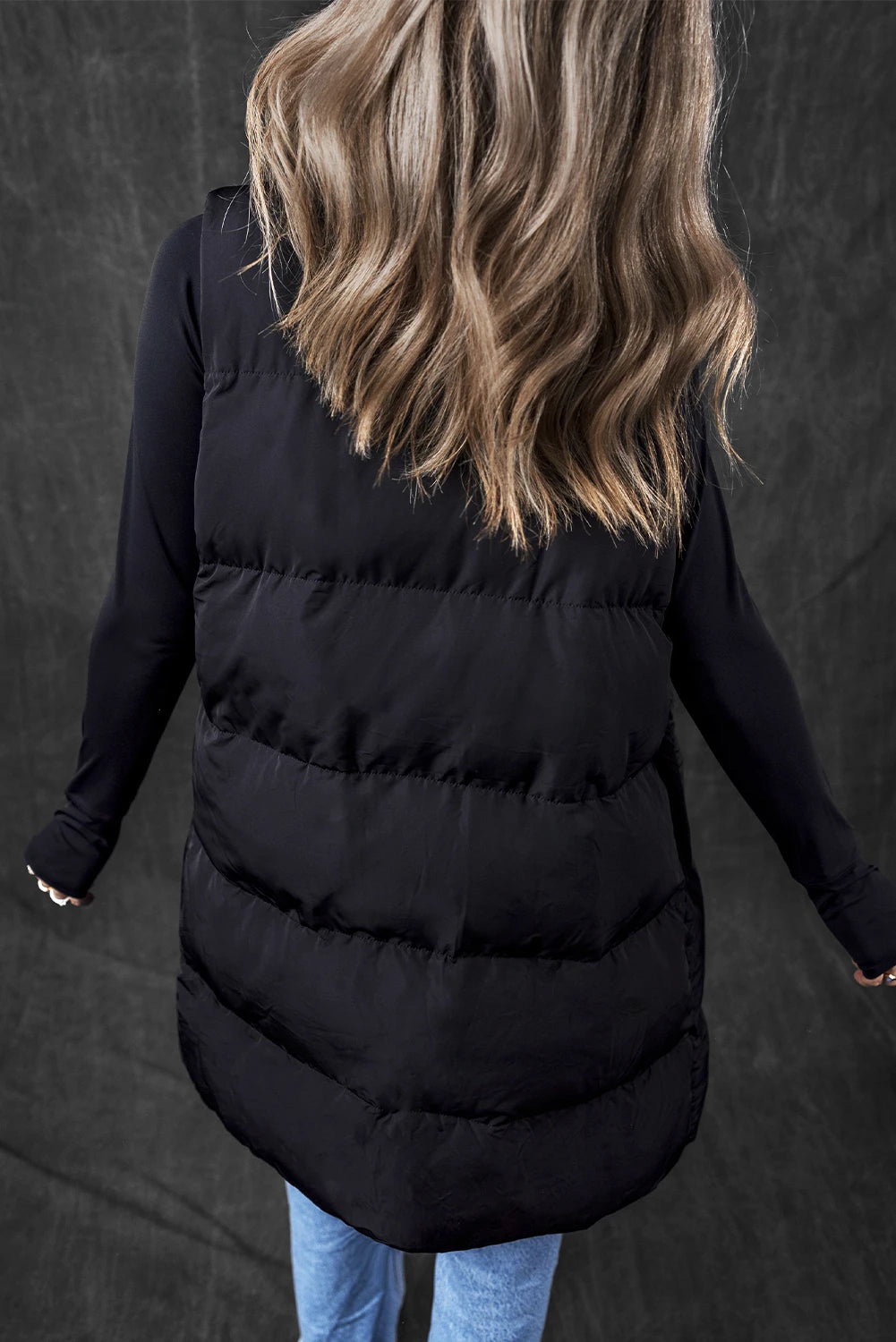 Person wearing a black puffer vest against a dark background