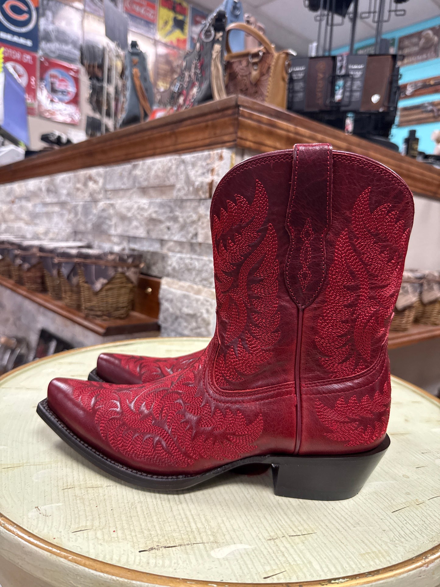 Red embroidered cowboy boot on a wooden block with a store interior in the background