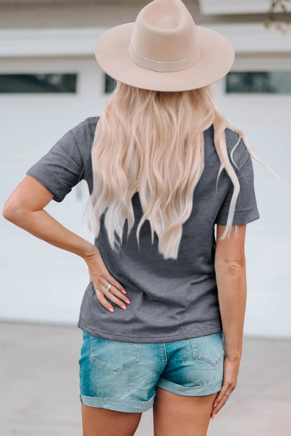 Person wearing a gray t-shirt and denim shorts with a beige hat, standing against a neutral background.