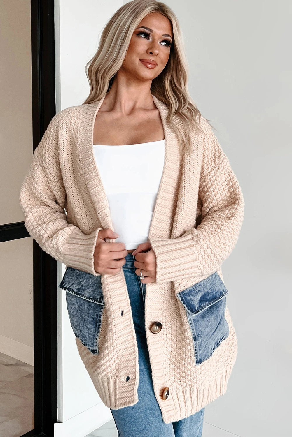 Woman wearing a beige knitted cardigan over a white top and blue jeans.