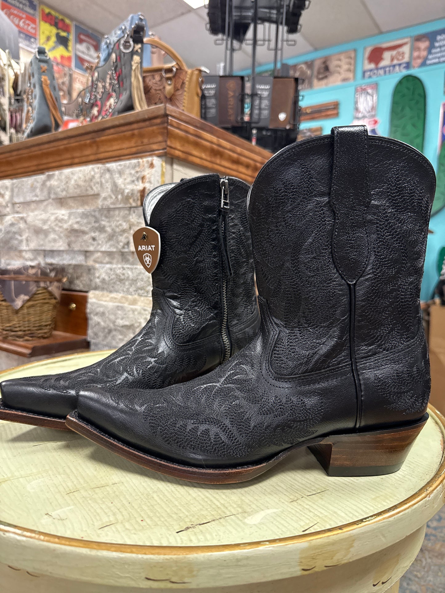 Black leather cowboy boots with brown soles on a wooden surface.