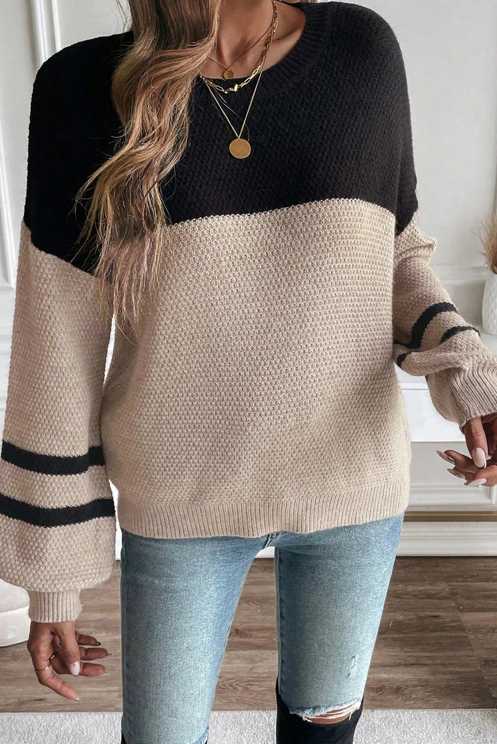 Person wearing a black and beige sweater with distressed jeans indoors.