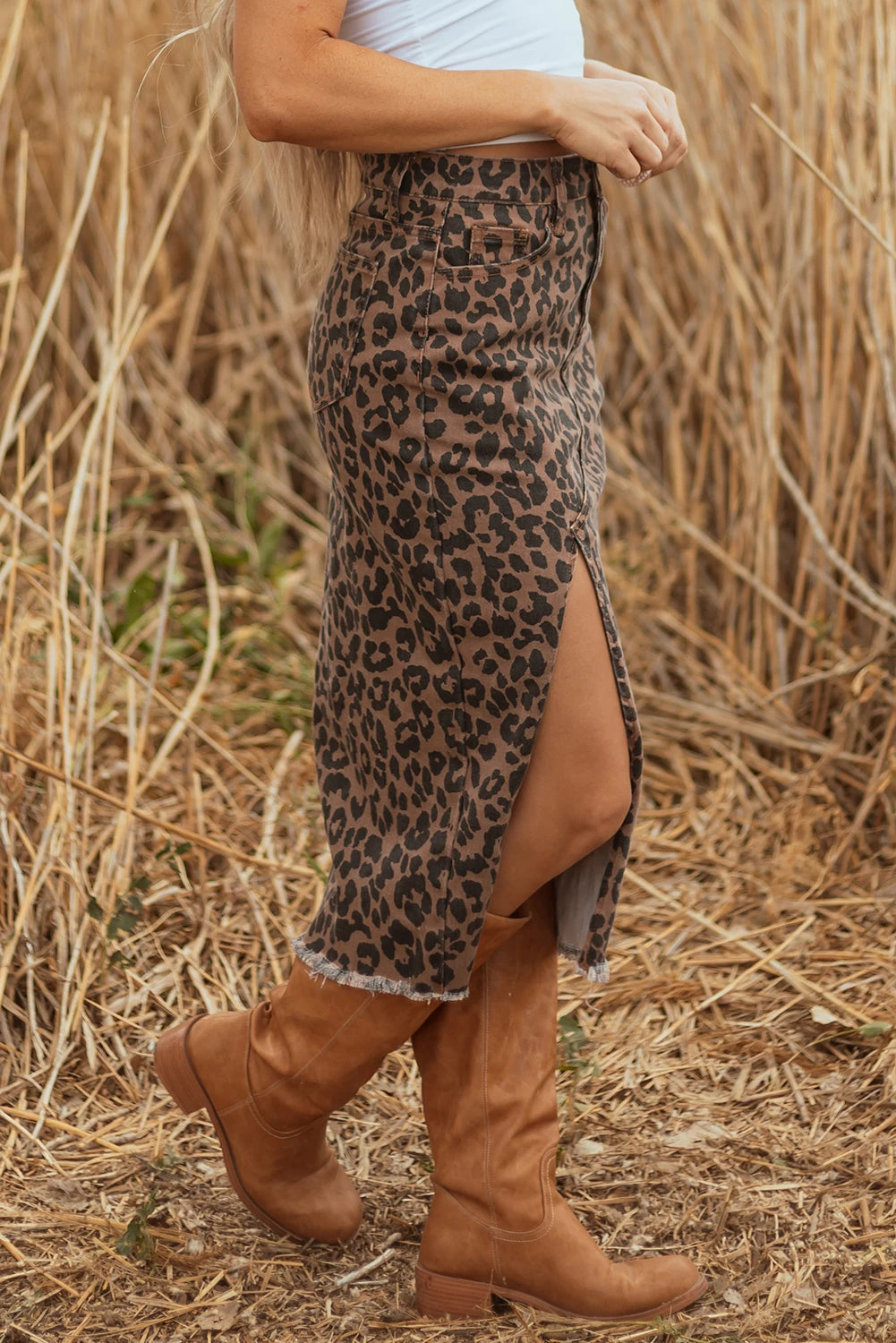 Person wearing a leopard print skirt and brown boots in a dry grass field