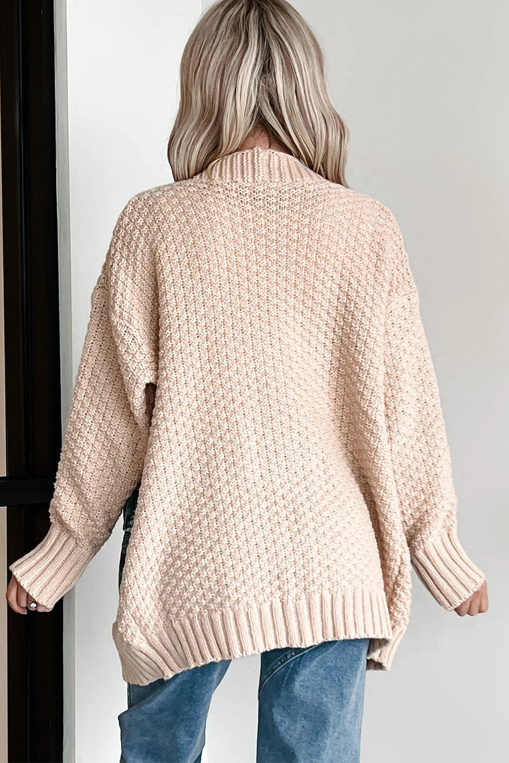Person wearing a beige knitted sweater and blue jeans against a white background