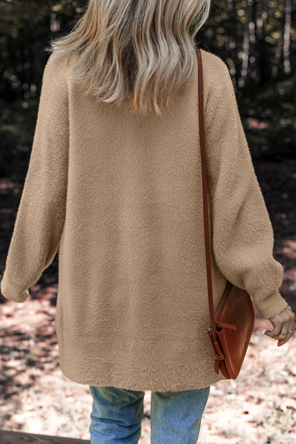 Person wearing a beige sweater holding a brown bag outdoors.
