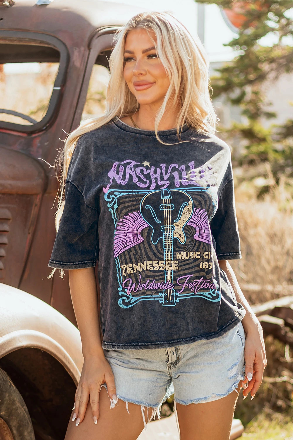 Woman wearing a graphic t-shirt with text and graphics, standing in front of an old truck.