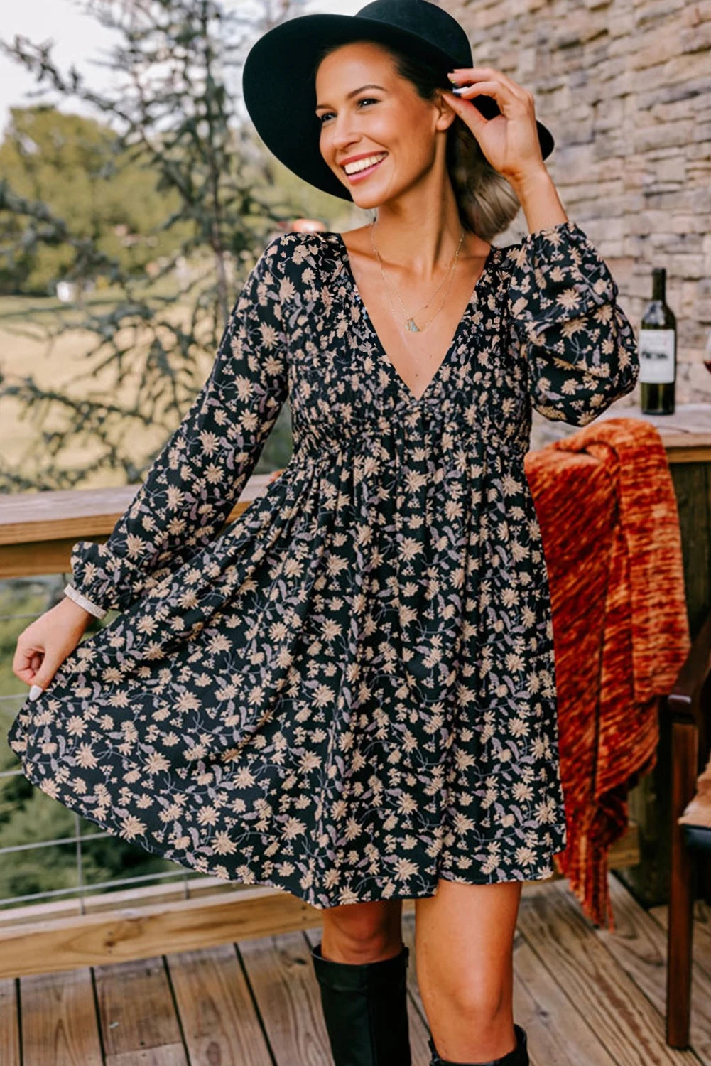 Woman in a floral dress and black hat standing on a wooden deck.