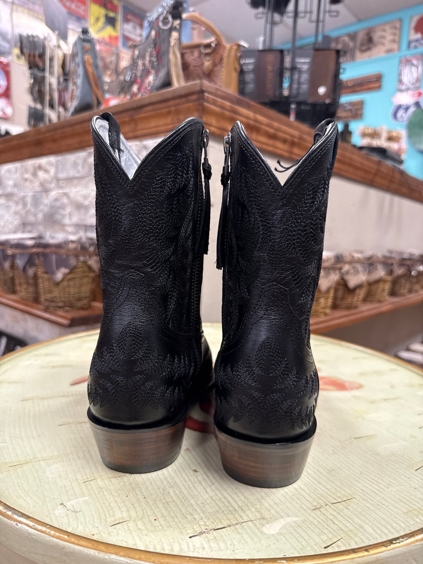 Black cowboy boots on a round wooden surface with a blurred indoor background