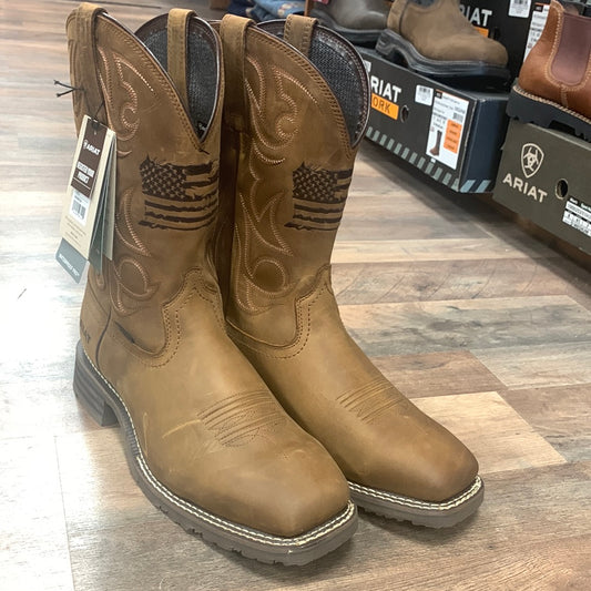 A pair of brown Hybrid Patriot Waterproof Western Boots with American flag embroidery on the shaft, displayed in a store setting.