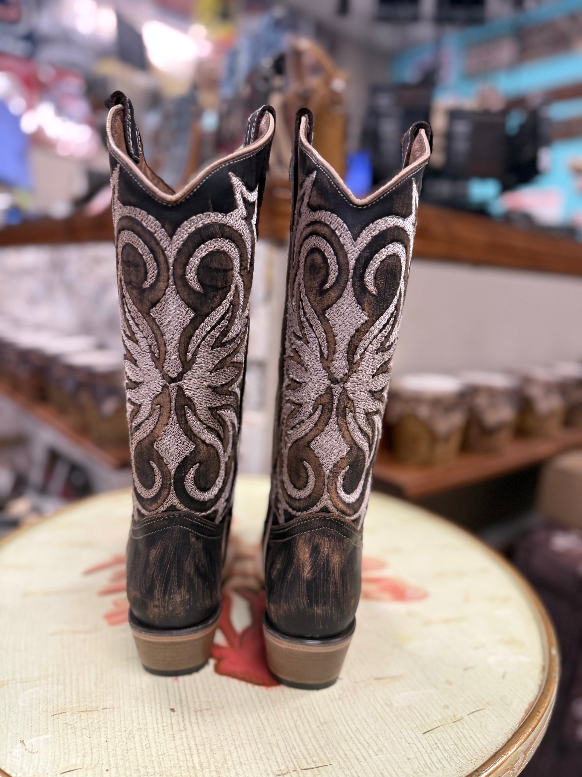Pair of cowboy boots with intricate designs on a round surface.
