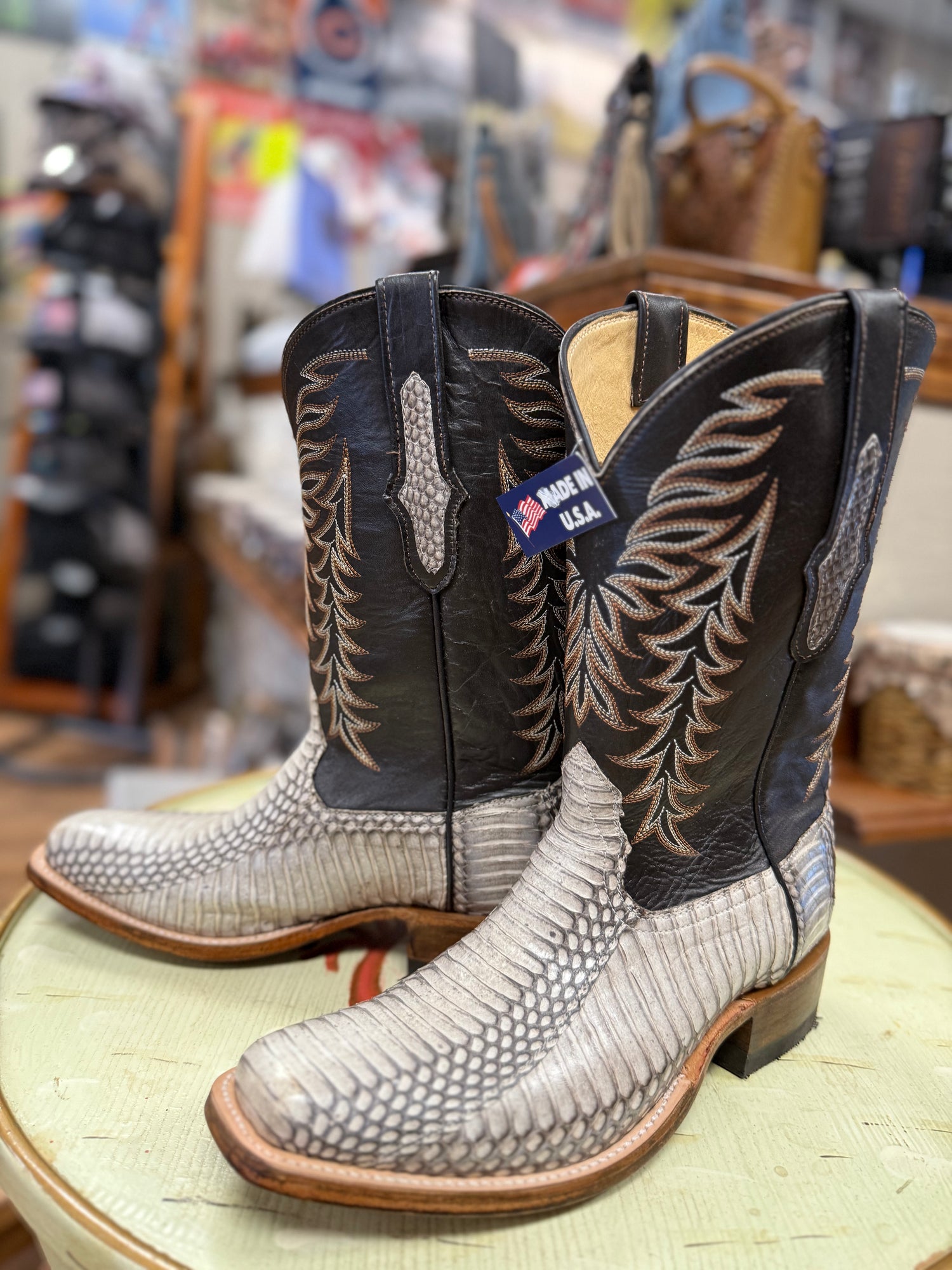 Pair of cowboy boots with detailed design on a round surface in a store setting.