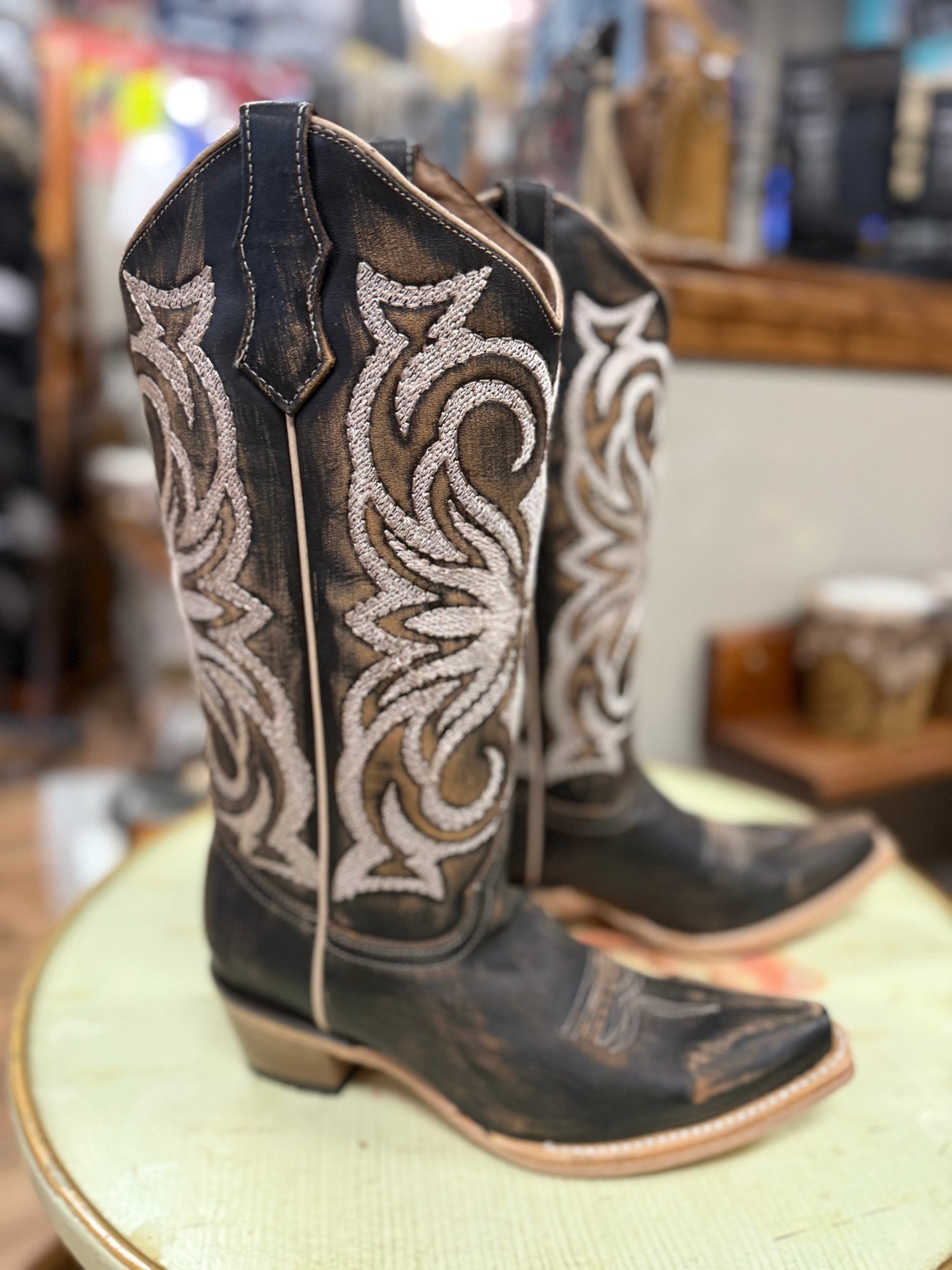 Pair of cowboy boots with intricate white embroidery on a green cushion