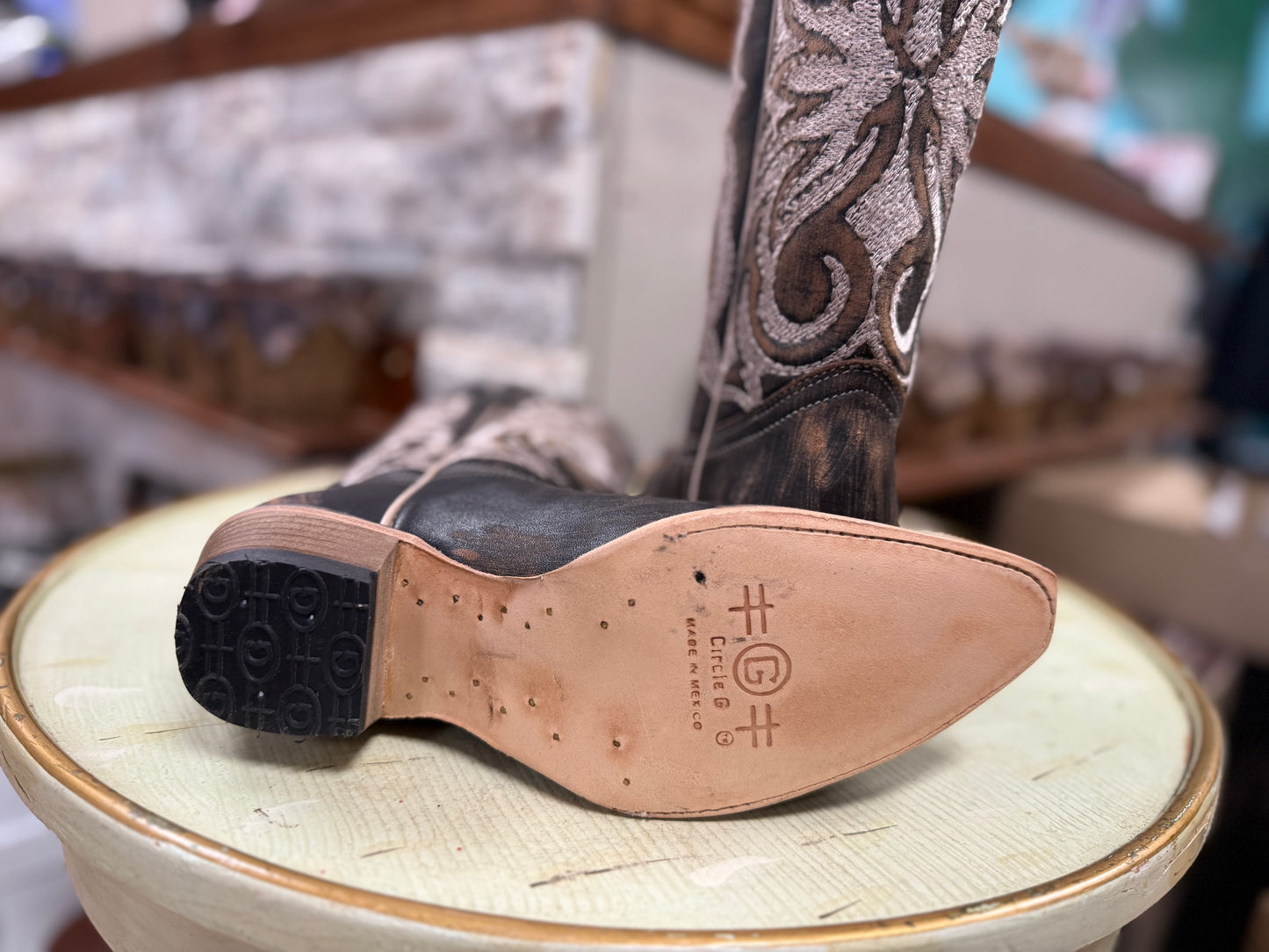Close-up of a brown leather boot with intricate design on a light green stool.