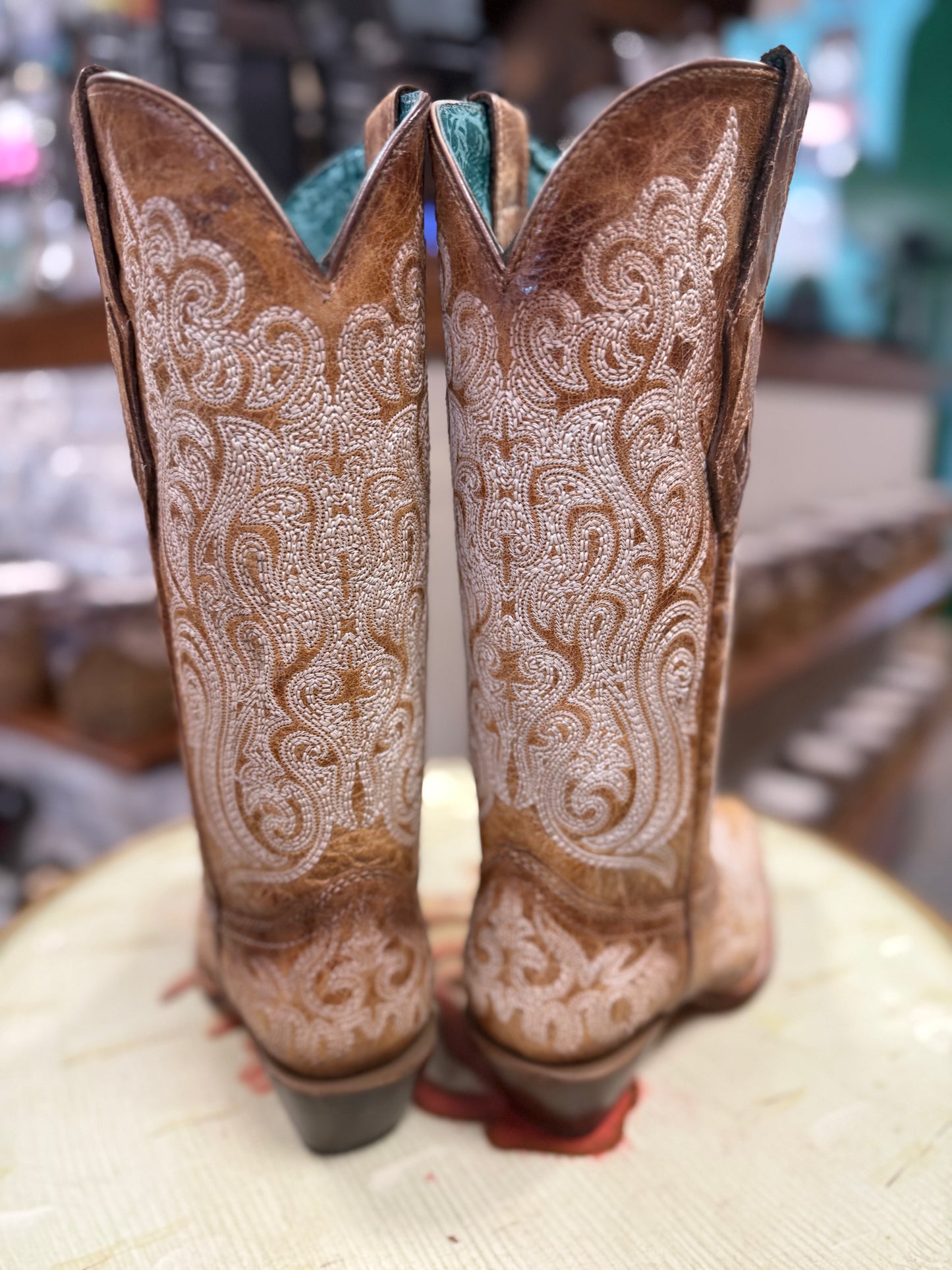 Pair of brown cowboy boots with intricate white patterns on a light surface.
