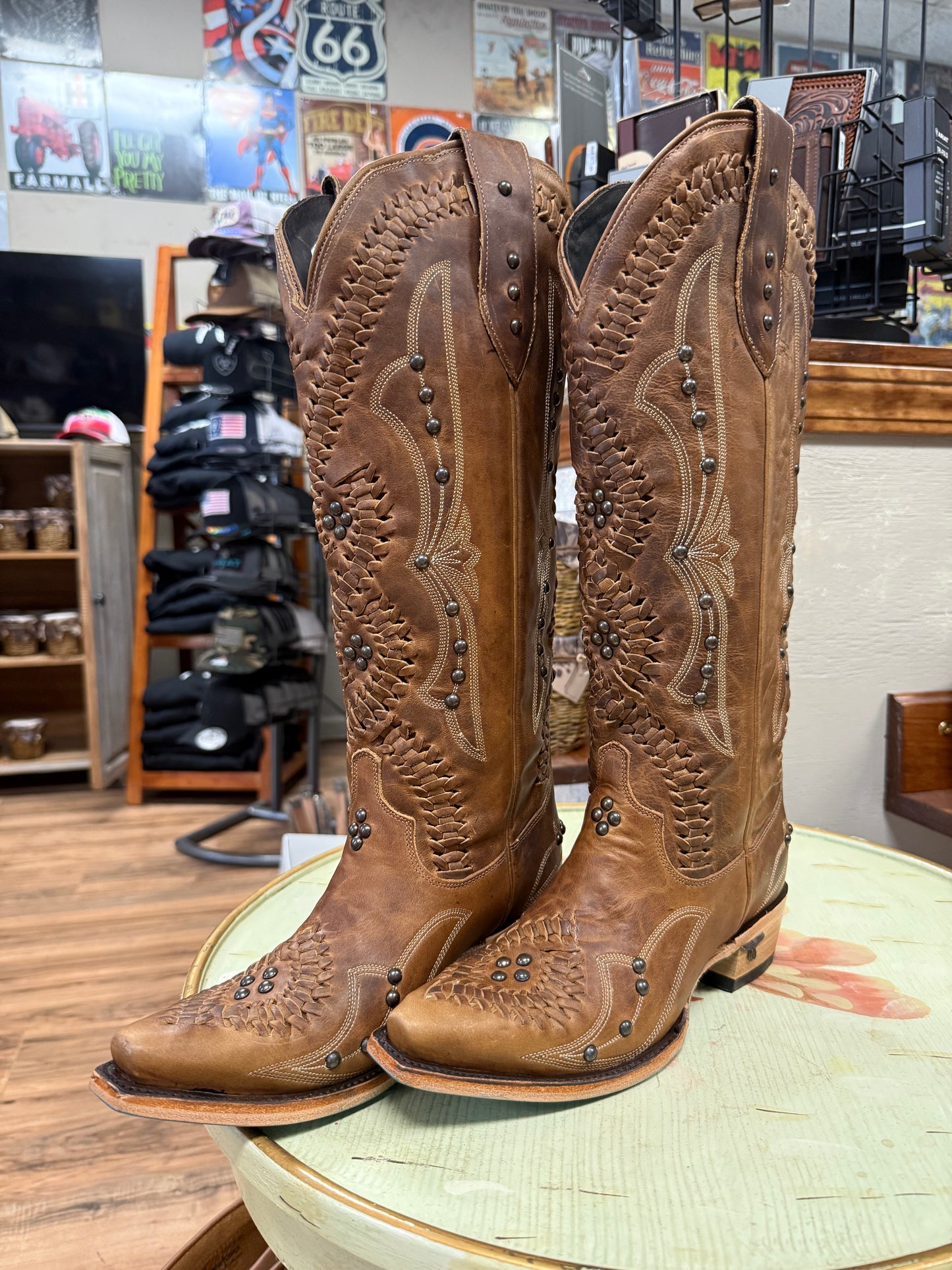 Pair of brown cowboy boots with intricate designs on a table in a store setting.