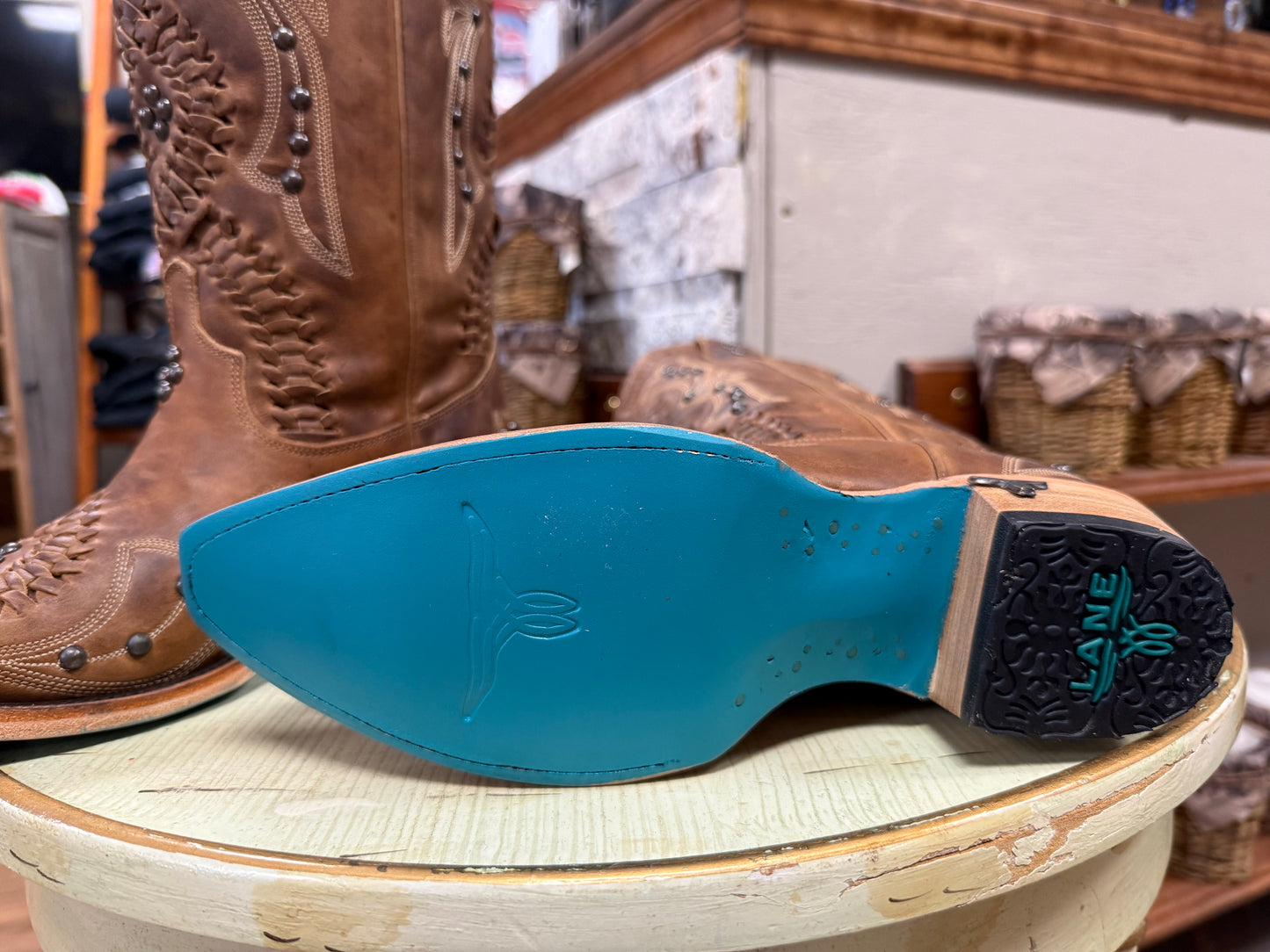Brown leather boot with a blue sole on a wooden surface, with a store interior in the background.