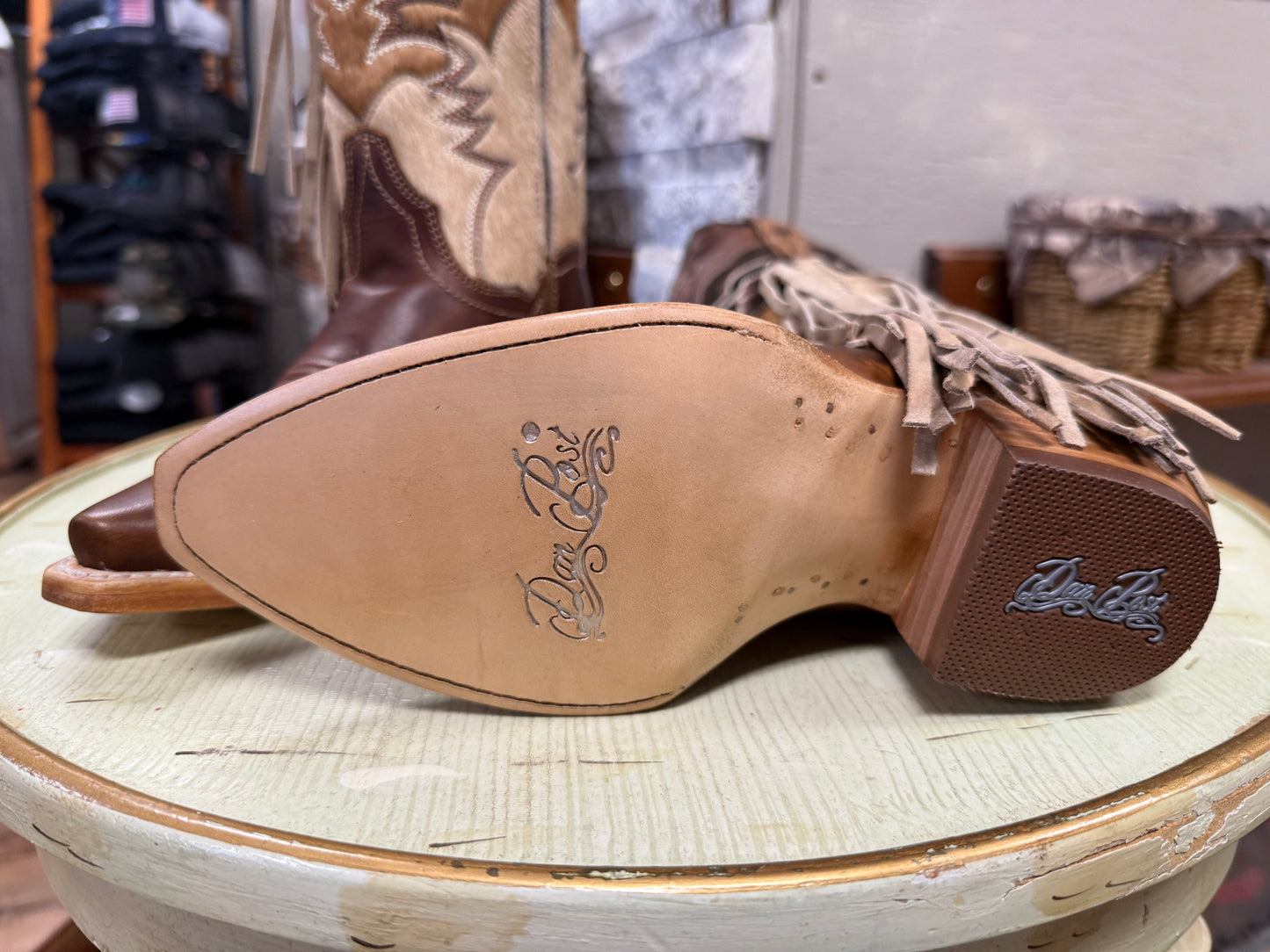 Close-up of cowboy boots with brand logo on the sole, placed on a textured surface.