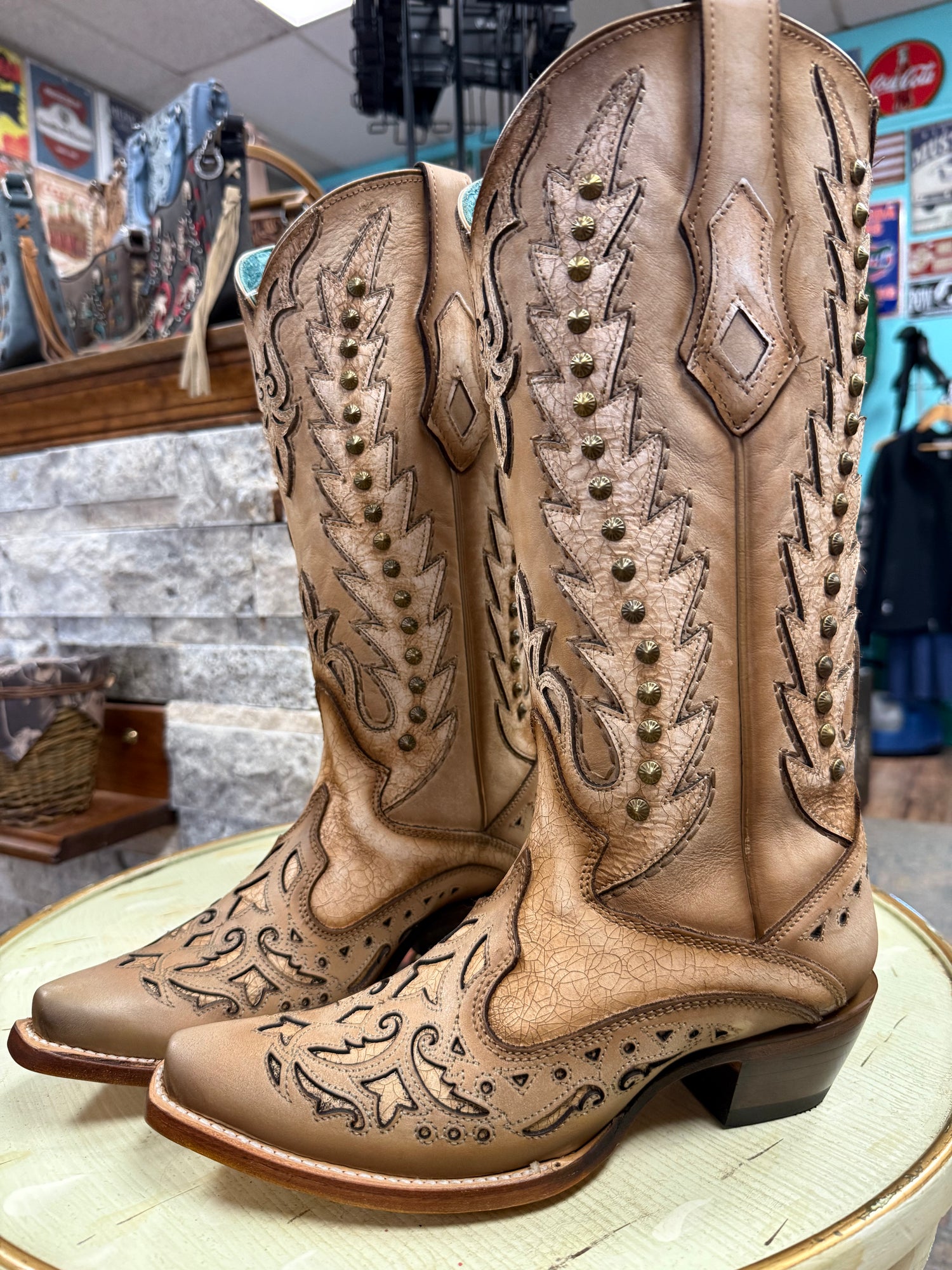 Pair of tan cowboy boots with intricate designs on a round surface.