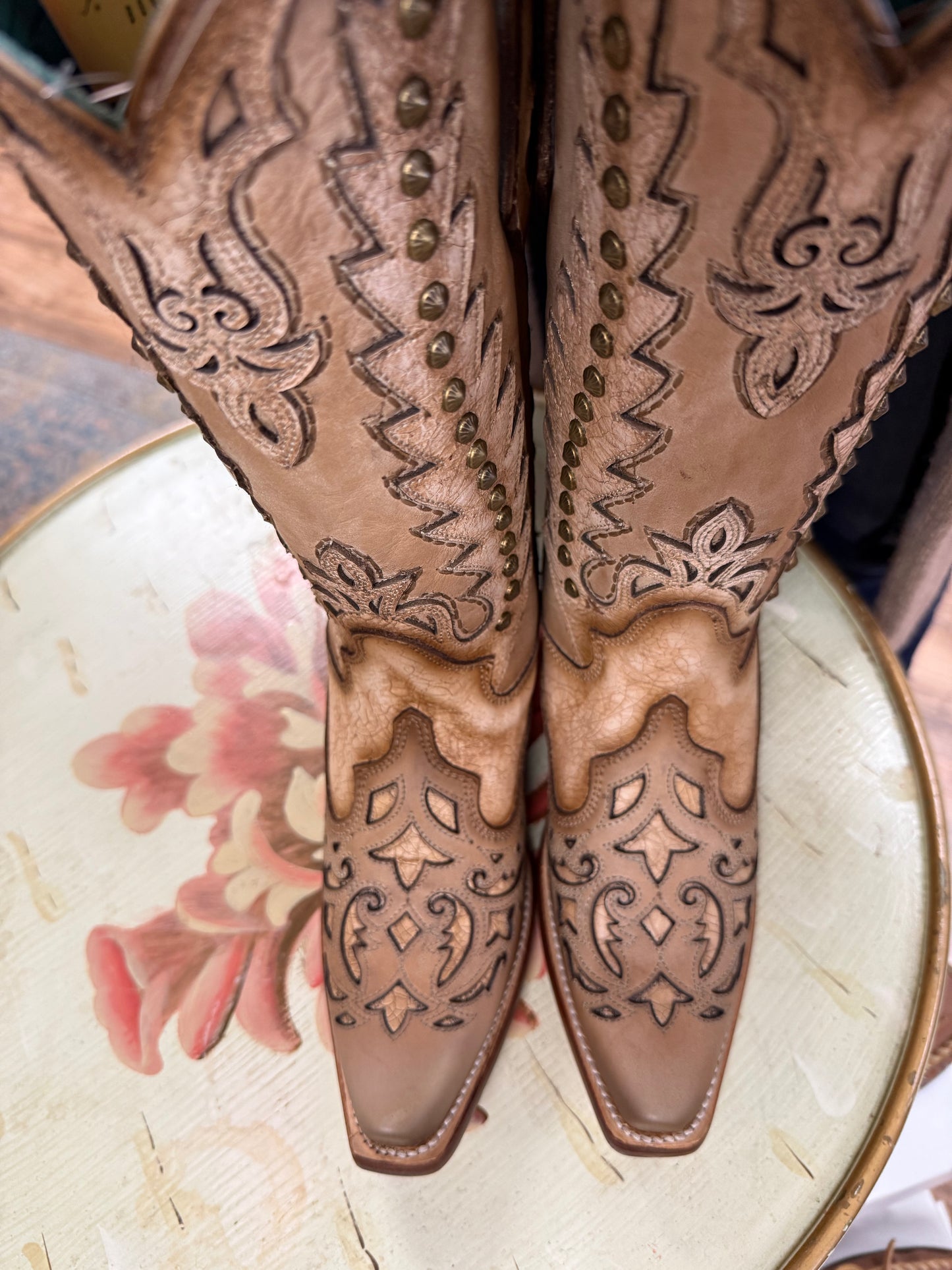 Pair of brown cowboy boots with intricate designs on a decorative plate.