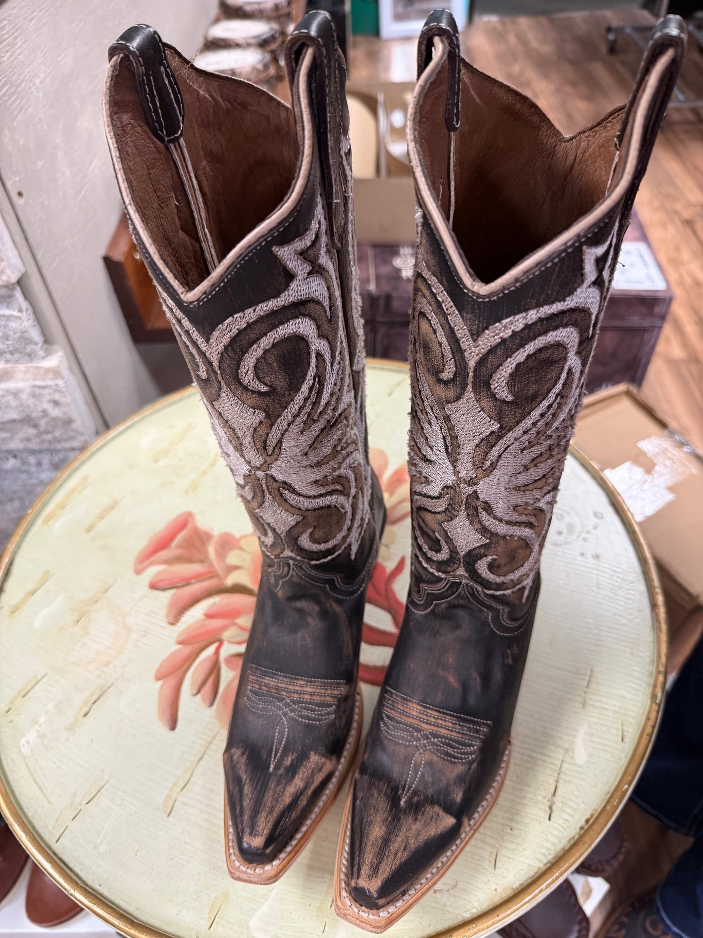 Pair of brown cowboy boots with intricate patterns on a round surface.