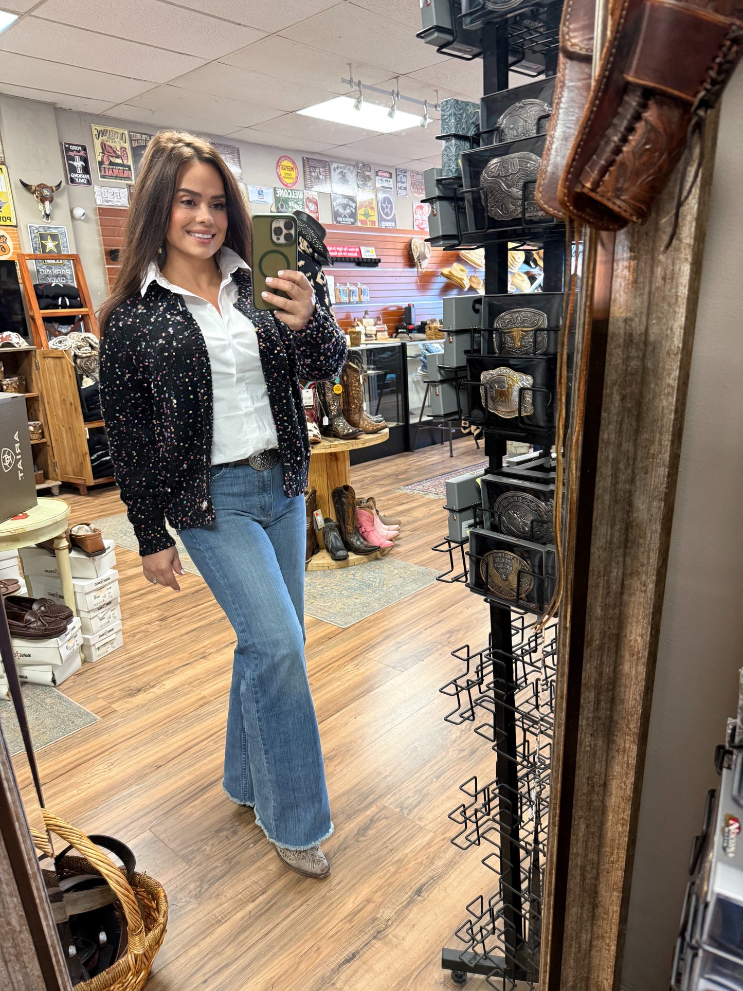 Woman taking a mirror selfie in a store with boots and decor on display.