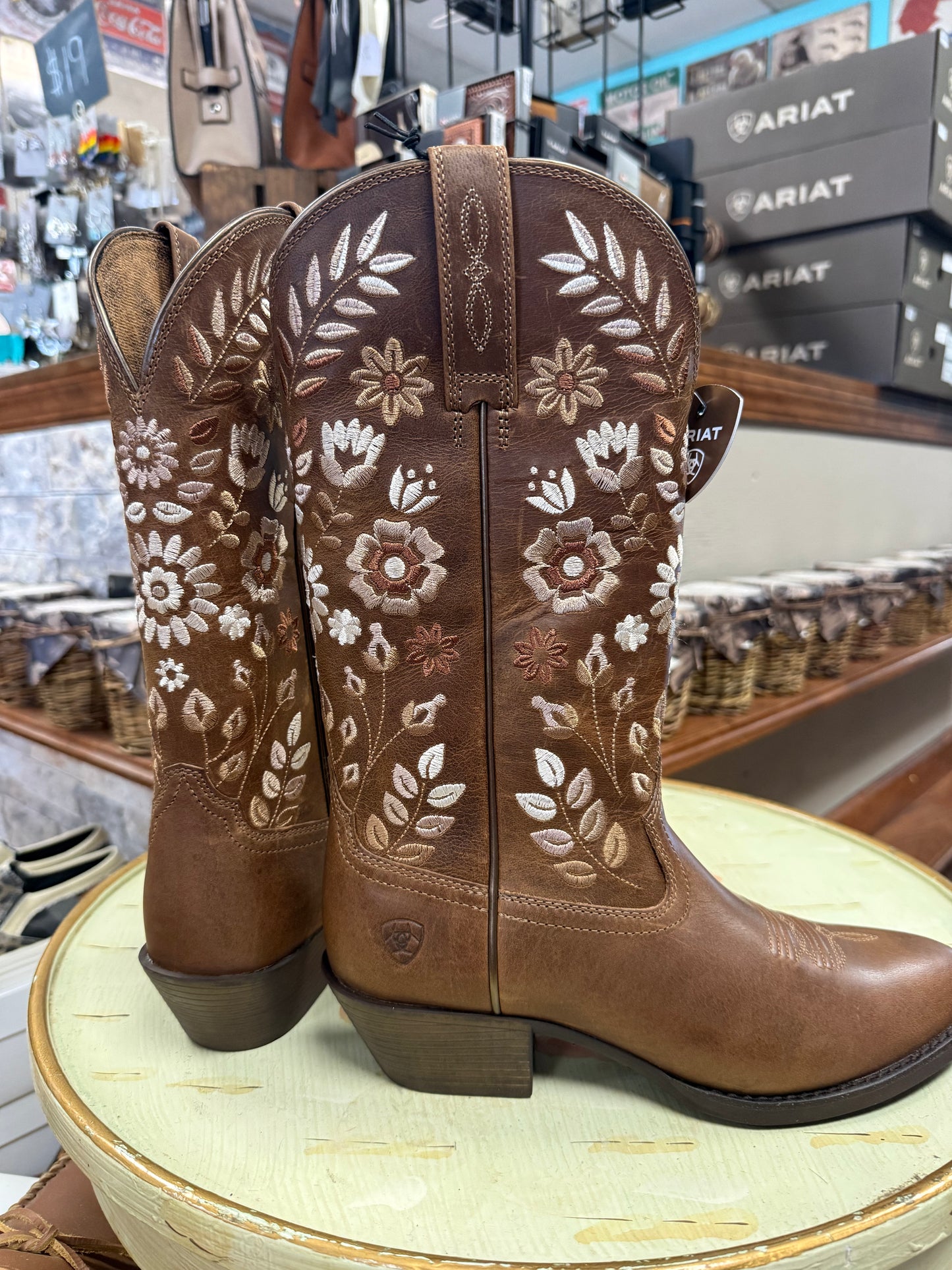 Brown cowboy boots with floral patterns on a round display table in a store setting.