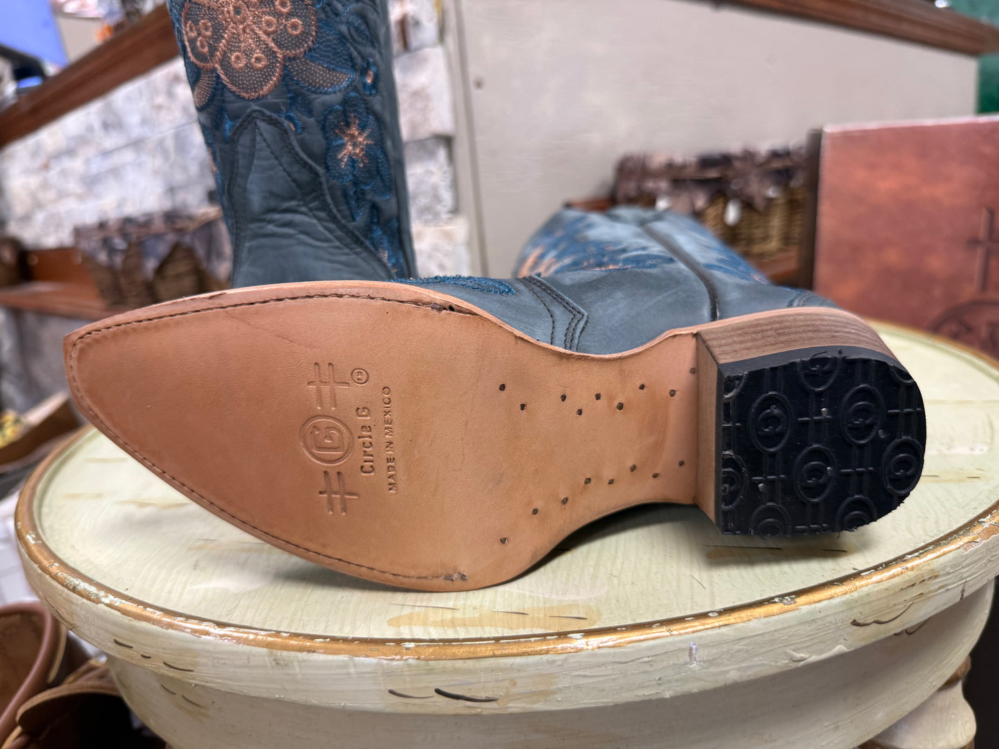 Close-up of a cowboy boot sole with brand logo on a wooden stool.