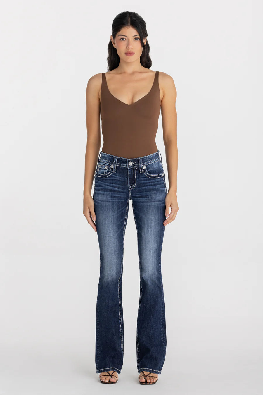 Woman wearing a brown tank top and blue jeans on a white background