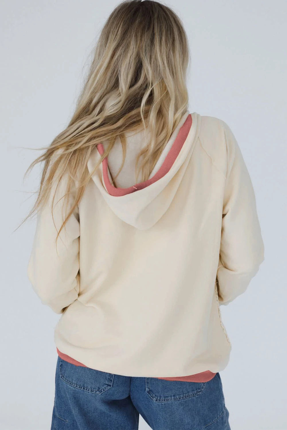 Person wearing a beige hoodie with a pink interior on a plain background