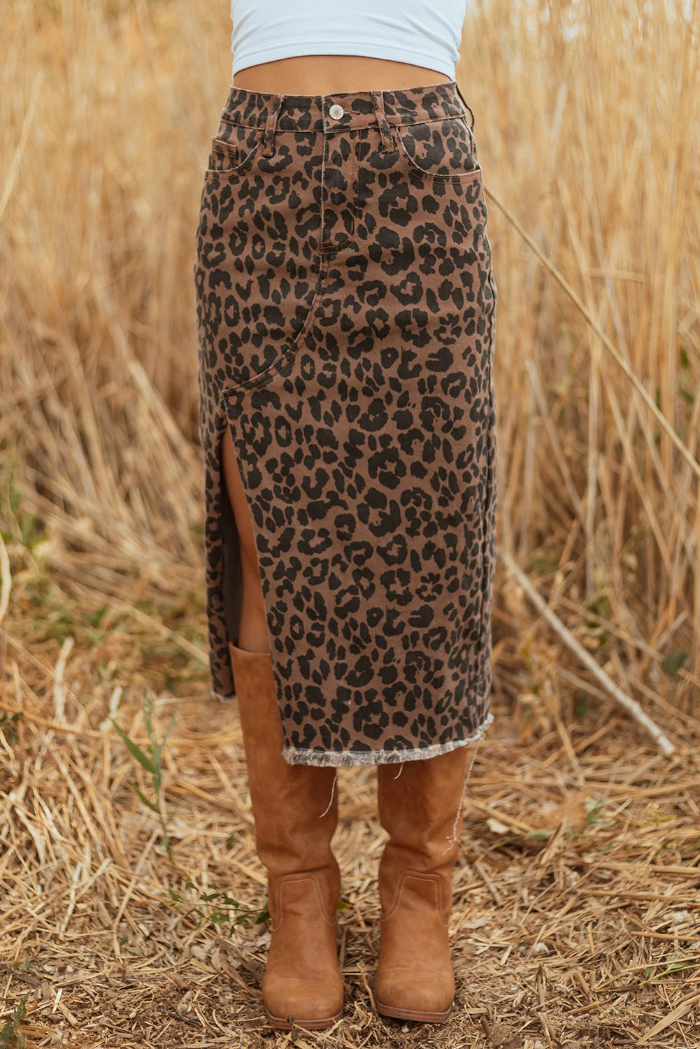 Person wearing a leopard print skirt and brown boots in a field of dry grass.