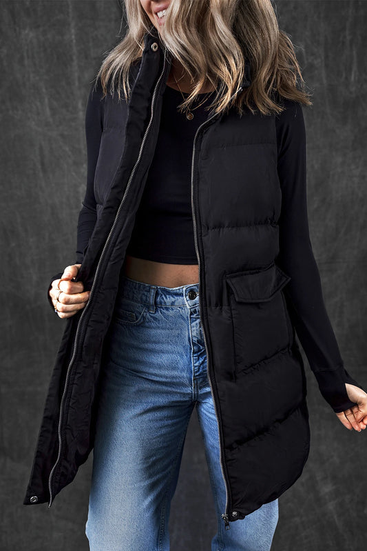 Person wearing a black puffer vest over a black top and blue jeans against a dark background