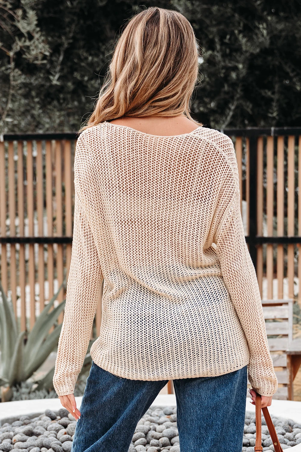 Woman wearing a beige knitted sweater and blue jeans standing outdoors.