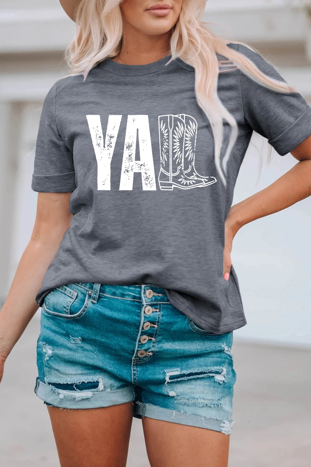 Person wearing a gray t-shirt with 'YA' and cowboy boot graphic, paired with denim shorts.