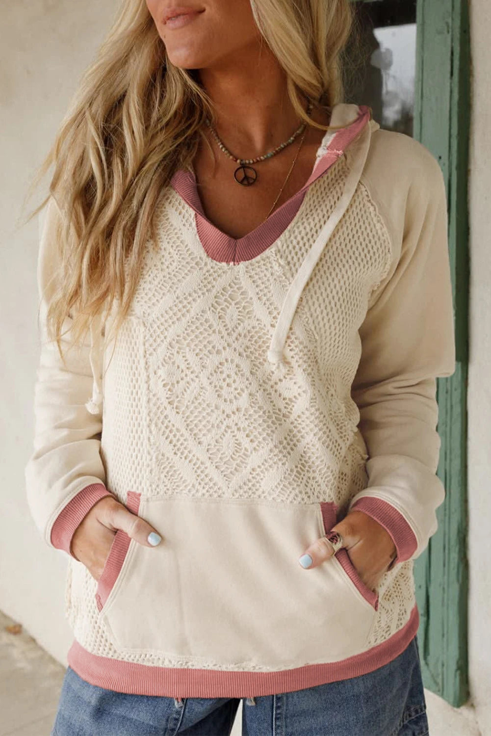 Woman wearing a cream and pink sweater with blue jeans, standing against a neutral background.