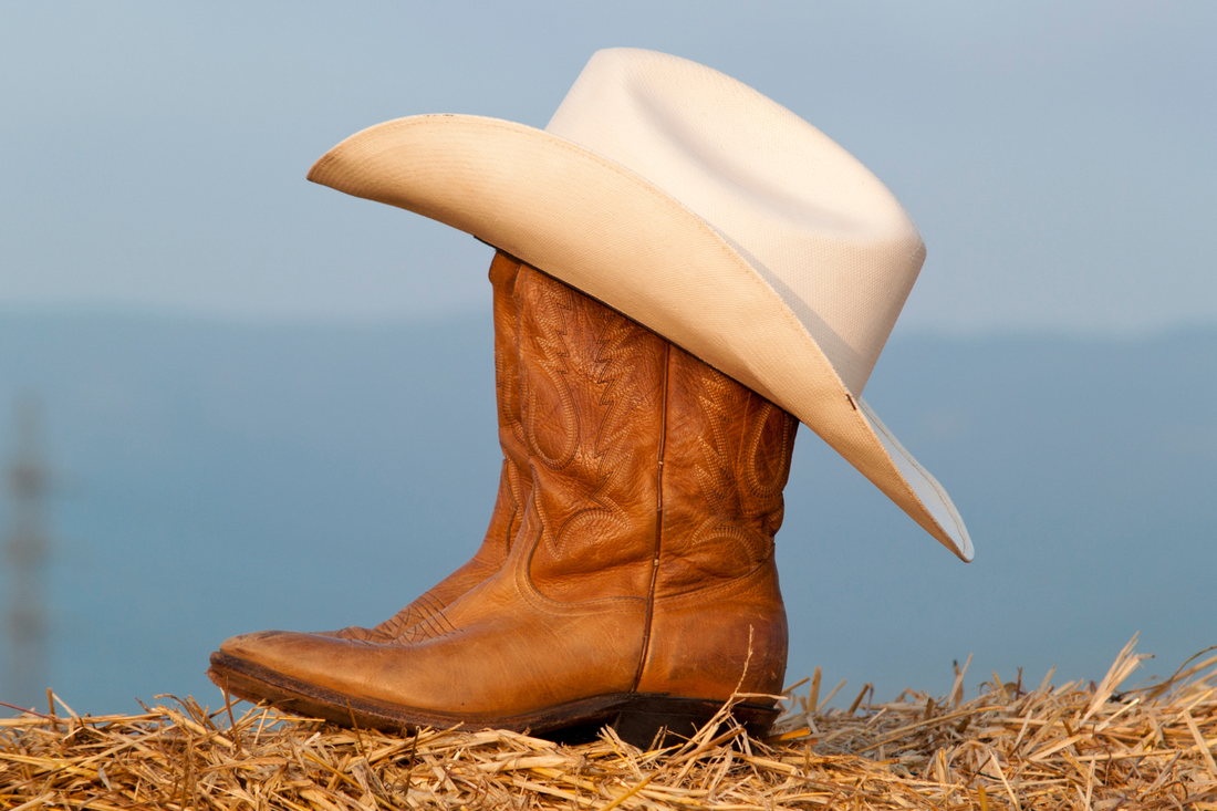 Brown leather cowboy boot with a white cowboy hat resting on top.