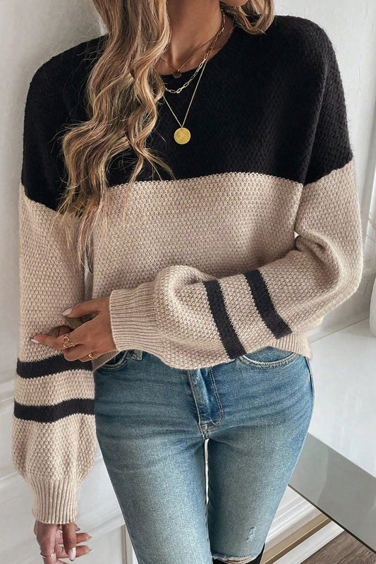 Person wearing a black and beige sweater with blue jeans indoors.