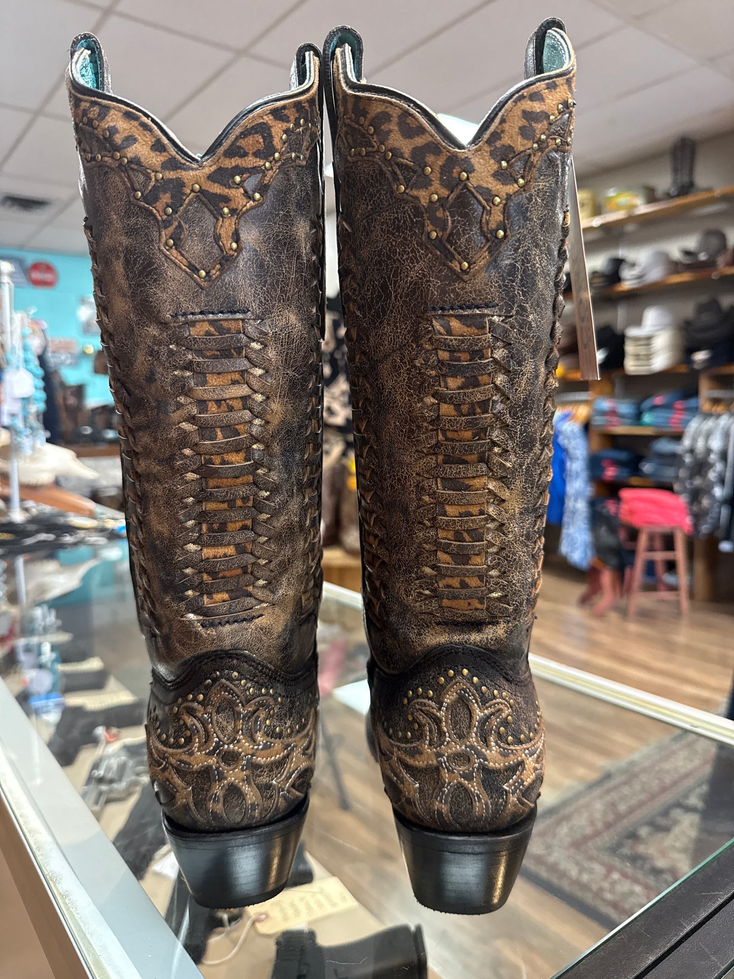 Pair of brown leather motorcycle grips with intricate designs on a blurred store background.